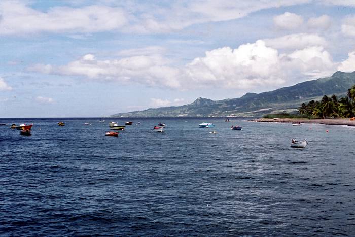 Blick über ein Meer, in dem viele kleine Boote schwimmen. Im Hintergrund eine Bergkette, die zum Meer hin abfällt.