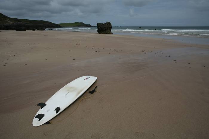 Ein Surfbrett liegt auf einem Strand mit dunklen Felsen.