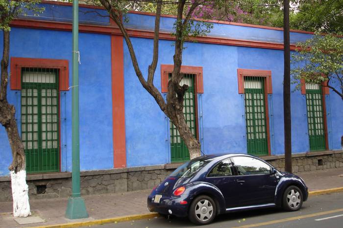 Ein VW-Käfer steht auf der Strasse vor einem blau angemalten Haus.