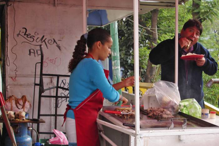 Eine junge Frau bereitet an einem Marktstand Essen zu. Ein Kunde schiebt sich gerade eine Fladenbrotrolle in den Mund.