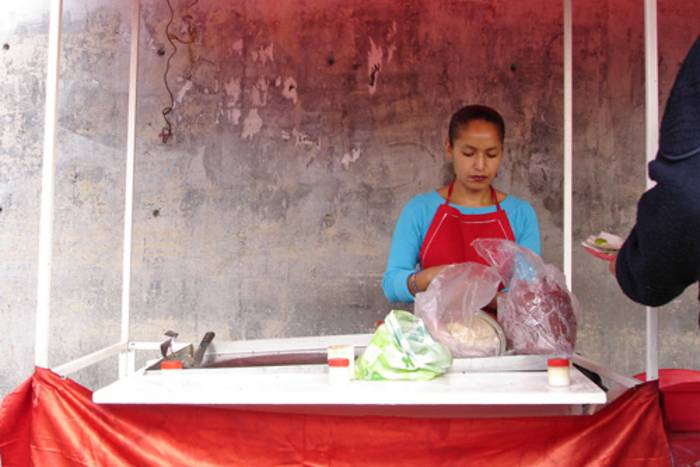Eine junge Frau hinter einem Marktstand, sie hat gefüllte Plastiktüten vor sich.