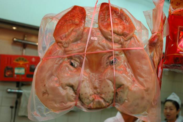 Ein Schweinekopf in einem Plastikbeutel, hängt an einem Verkaufsstand.