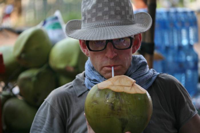 Ein Mann mit Hut trinkt mit Hilfe eine Halms aus einer Kokosnuss.